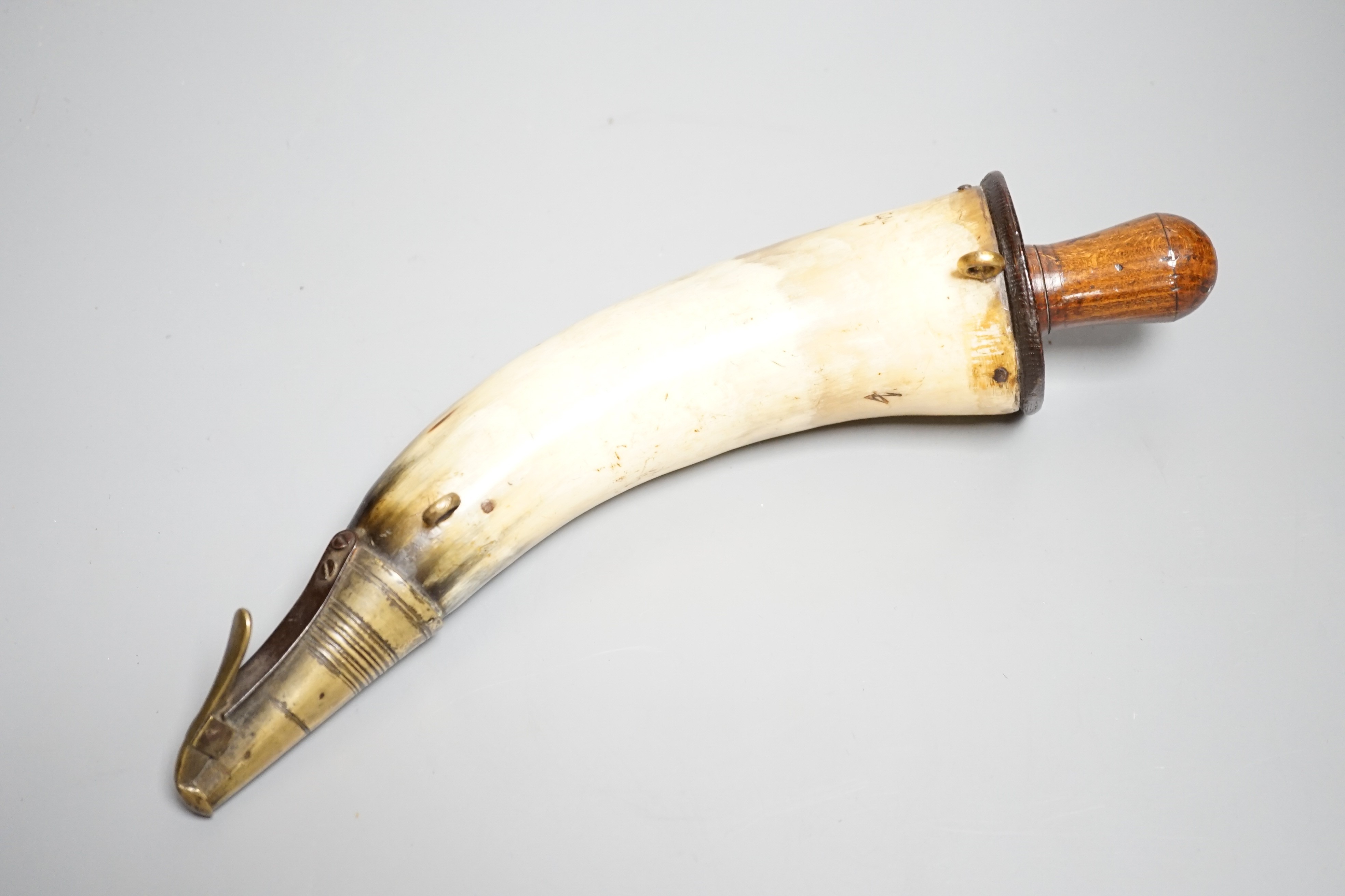 A British military Gunner's powder horn c.1800, cow horn body, sprung brass charger, wooden end cap and plug, two brass suspension rings, body branded with WD stamp and broad arrow. Length 29cms.